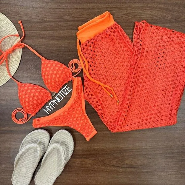 Orange bikini set with crochet-inspired fabric and 'HYPNOTIZE' waistband detail, paired with a matching cover-up and laid out with a straw hat and white sandals for a complete beach-ready look.